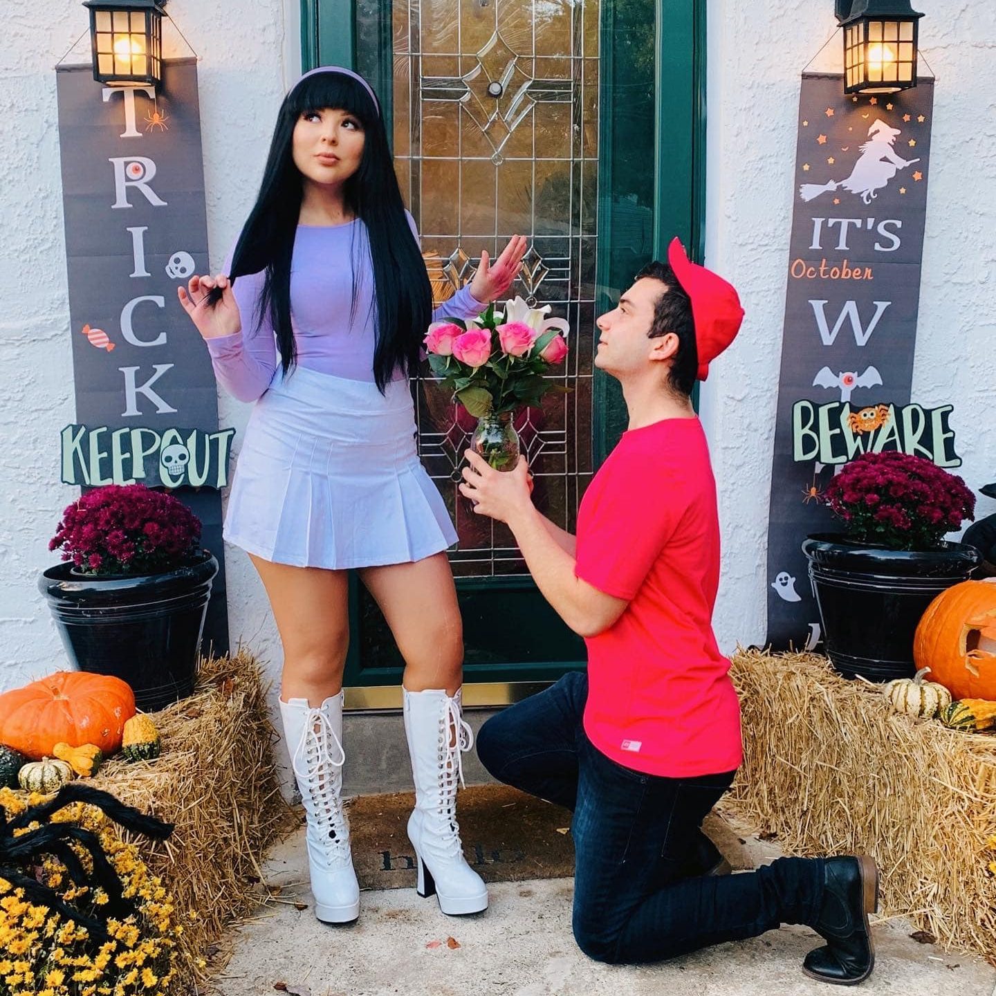 Person kneels offering flowers, another stands dismissively; pumpkin decorations and Halloween-themed banners in a front porch setting.
