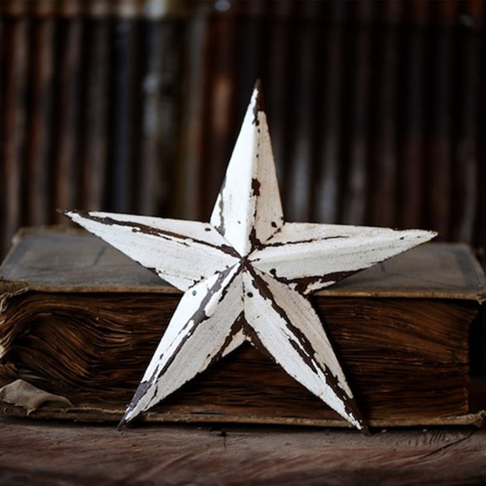 A rustic, metal star rests on a closed, old book with frayed pages, set against a dark, blurred wooden background.