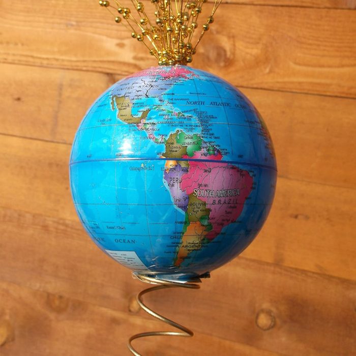 Globe mounted on a spring, adorned with gold wires, against a wooden background.