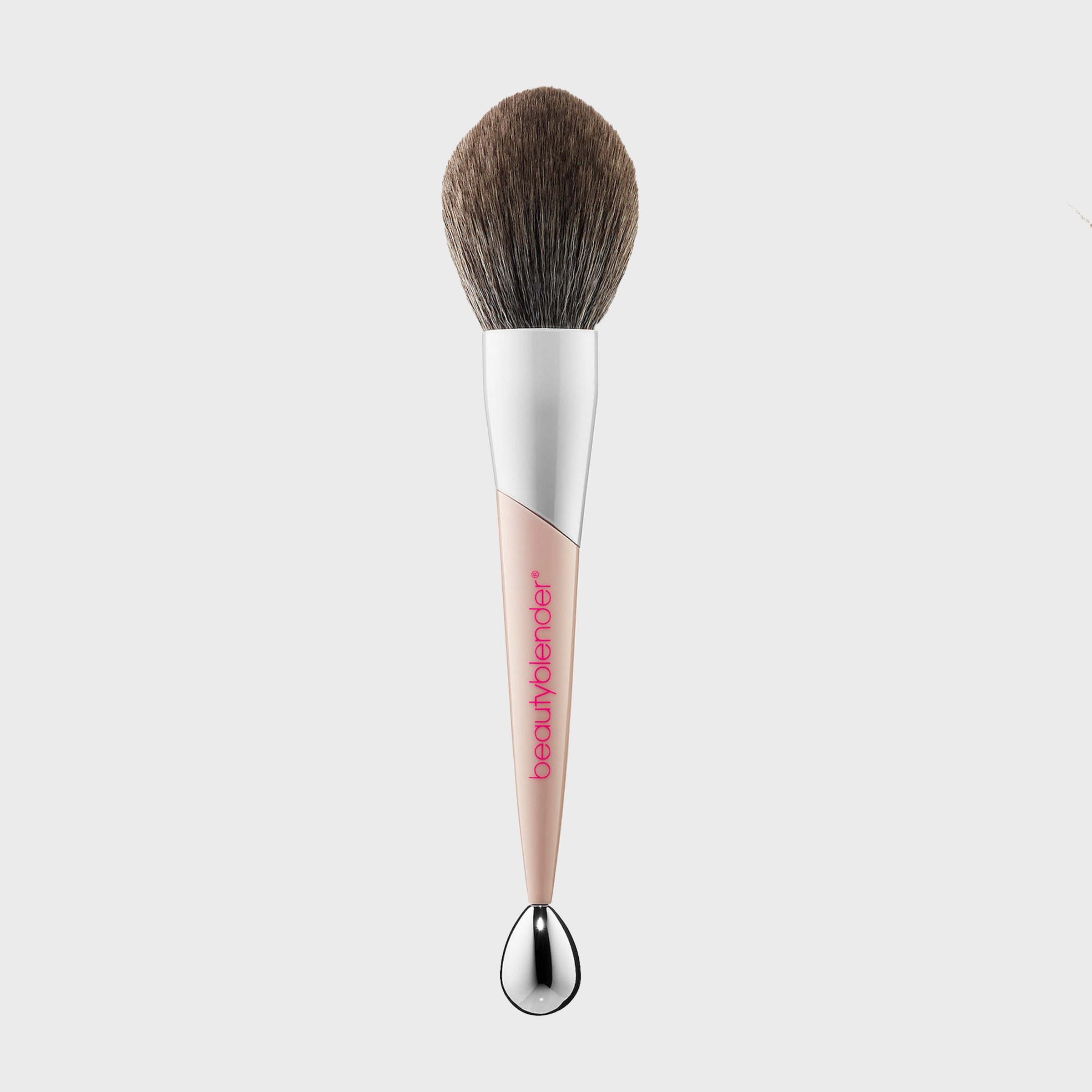 Makeup brush with a beige handle resting upright; brand "beautyblender" in pink; set against a plain white background.