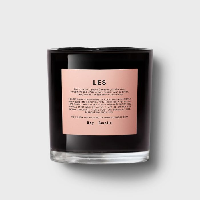 Black candle showcases label detailing scent notes and burn time, set against a plain background.