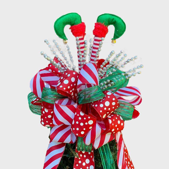 Festive Christmas bow features red, white, and green ribbons adorned with polka dots and stripes. Sparkly white embellishments and elf-like elements enhance the decoration.
