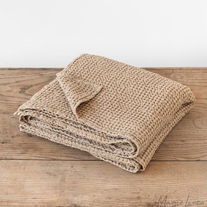 Folded beige waffle-textured blanket sits on a wooden surface, with a corner flipped open.