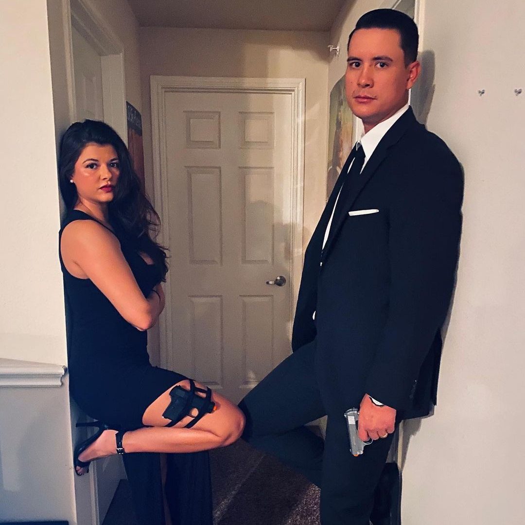 Two people pose confidently in a hallway; the woman sits with a holstered gun, the man stands holding a pistol.