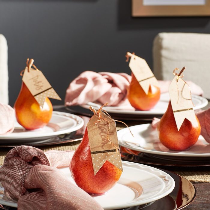 Pears with name tags sit on white plates, surrounded by pink cloth napkins, in a dimly lit dining setting.
