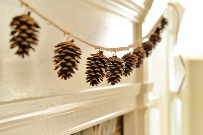 Pinecones hang on a string, decorating a mantel in a softly lit room.