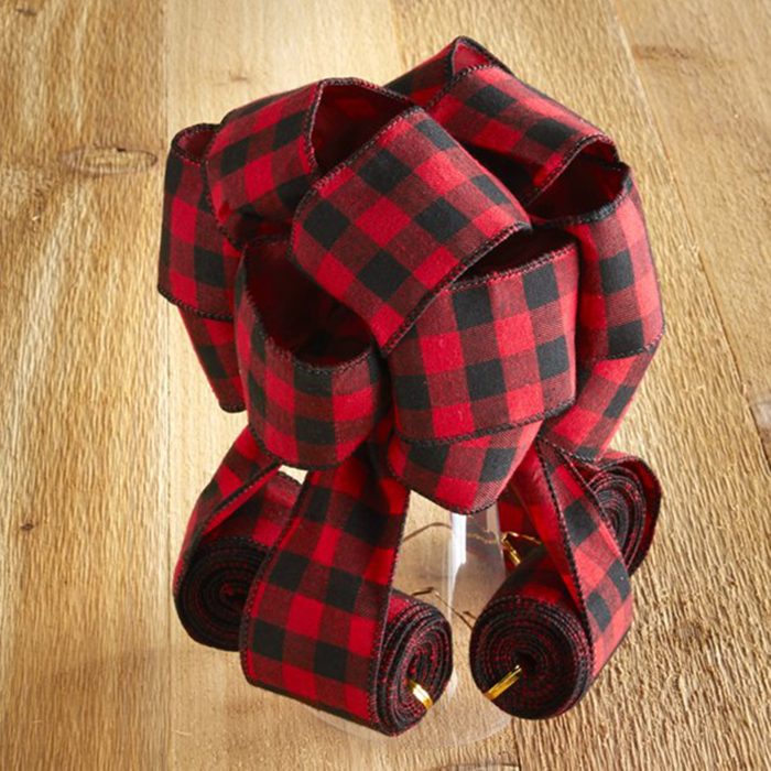 Red and black plaid ribbon forms a decorative bow on a wooden surface.