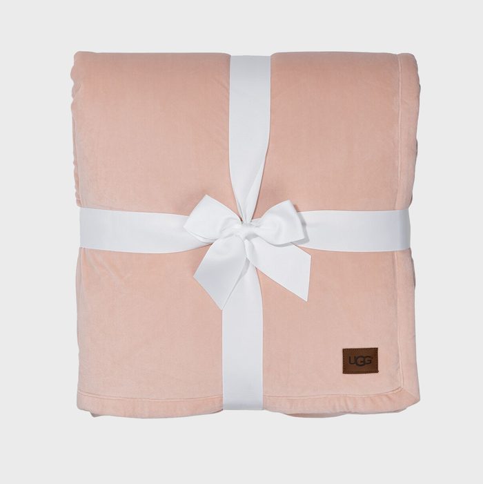 A folded pink blanket with a white ribbon bow is tied around it, featuring a small UGG brand tag in a neutral setting.