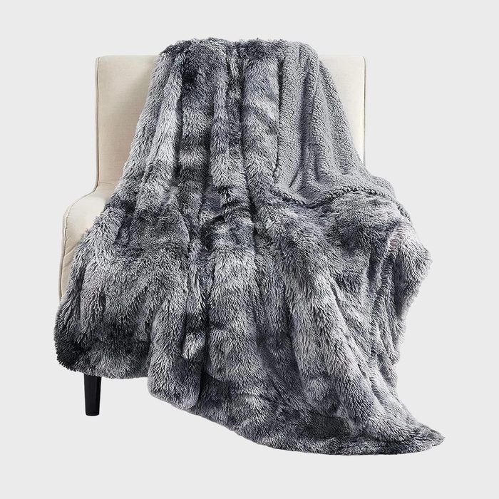 A plush, gray faux fur blanket drapes over a cream-colored armchair against a plain background.