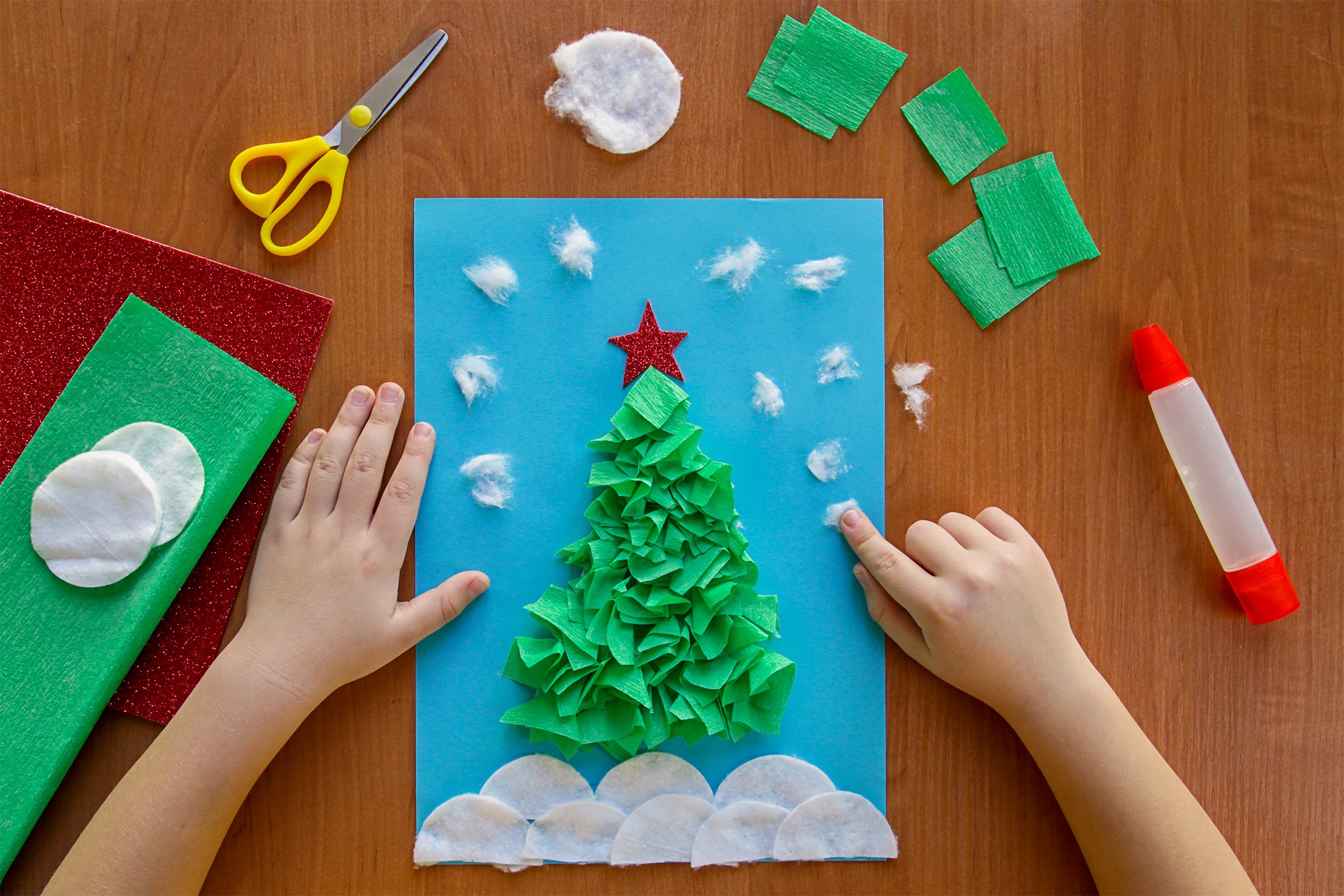 little child making winter decoration "Christmas Tree" from paper, crumpled paper or napkins, and cotton disc