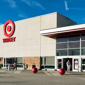 Target storefront features bold red logo; people walk outside. Red spheres line entrance against a backdrop of clear blue sky and brick walls.