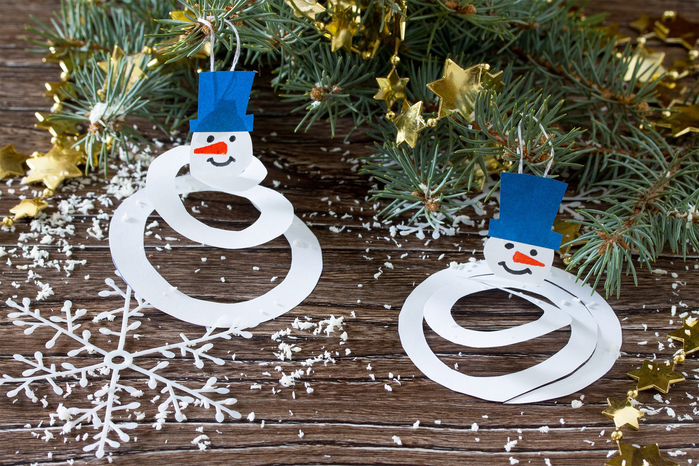 The child makes a toy on the Christmas tree snowman paper. Glue, paper, scissors on a wooden table.