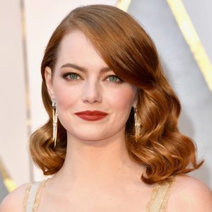 A woman with red hair smiles slightly, wearing long earrings, in a formal setting with a neutral background.