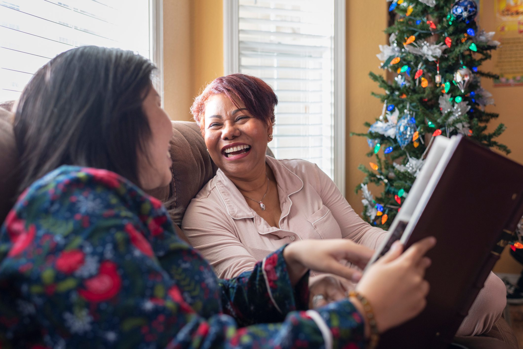 Mother and daughter looking at photo album near Christmas tree