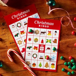 Bingo cards displaying Christmas symbols lay on a wooden table, surrounded by ornaments, candy canes, and scattered red and green candies.