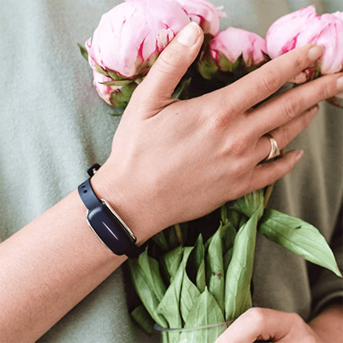 Hand grasping a bouquet of pink peonies, wearing a black fitness tracker; set against a neutral background.
