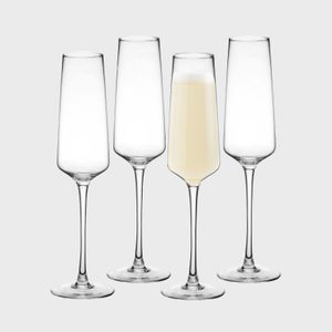 Four tall champagne flutes are standing upright; one is filled with a light sparkling beverage, set against a plain gray background.