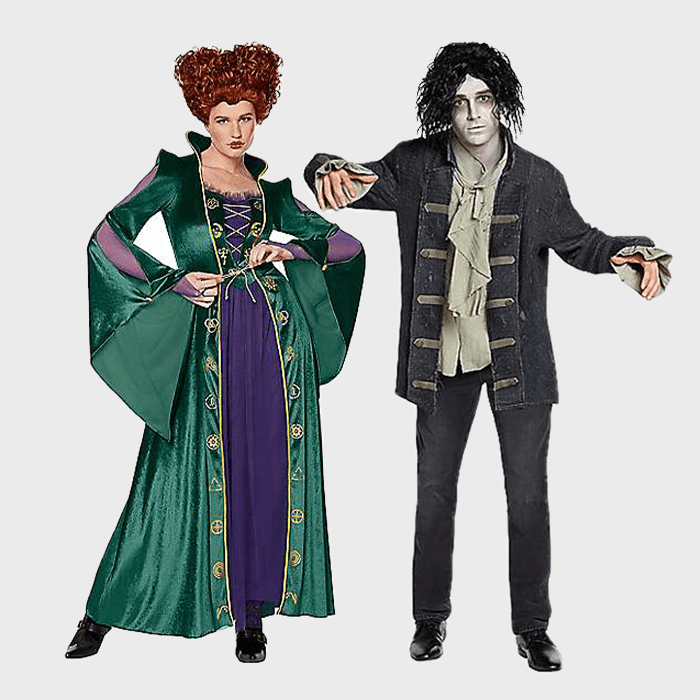 Two adults wear Halloween costumes; one as a witch in a green robe, the other as a zombie in tattered clothes. They're posing together.