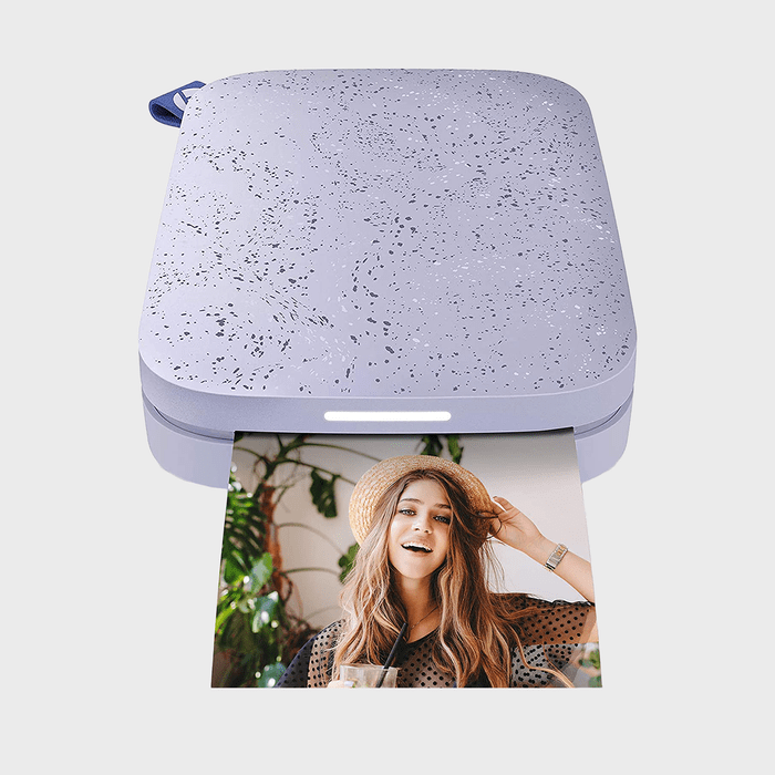 A speckled printer prints a photo of a smiling woman in a hat, surrounded by plants.
