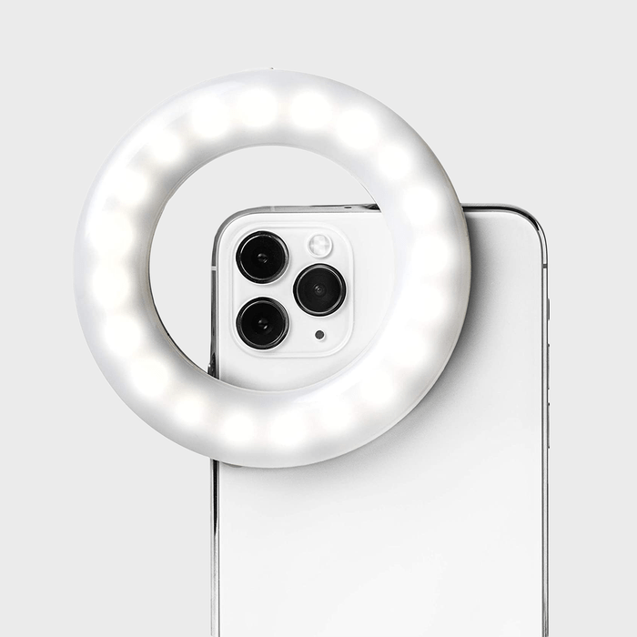 A smartphone is fitted with a glowing ring light, illuminating its camera, against a plain gray background.