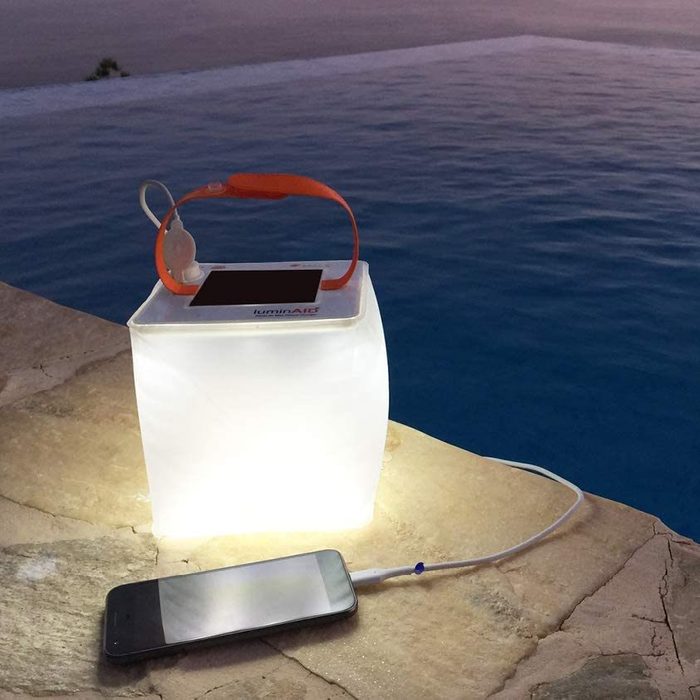 A glowing lantern charges a phone on a poolside stone ledge at dusk.