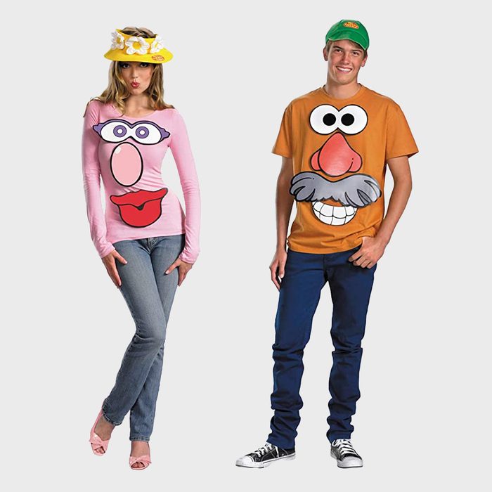 Two people stand, wearing novelty shirts featuring cartoon faces. One wears a pink shirt and hat, the other an orange shirt and green cap.