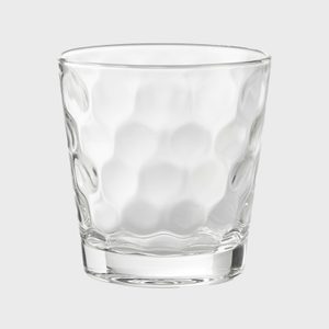 A textured glass with a dimpled surface stands, empty, against a plain, light gray background.