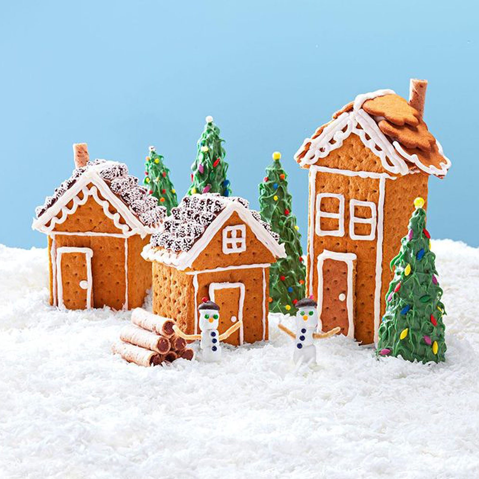 Gingerbread houses stand amidst frosting snow, surrounded by decorated trees and two snowmen, creating a festive winter scene.