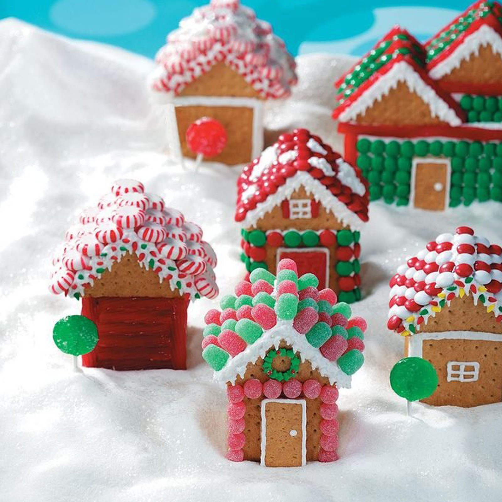Gingerbread houses decorated with colorful candies sit on a snowy surface, creating a festive, winter-themed scene.