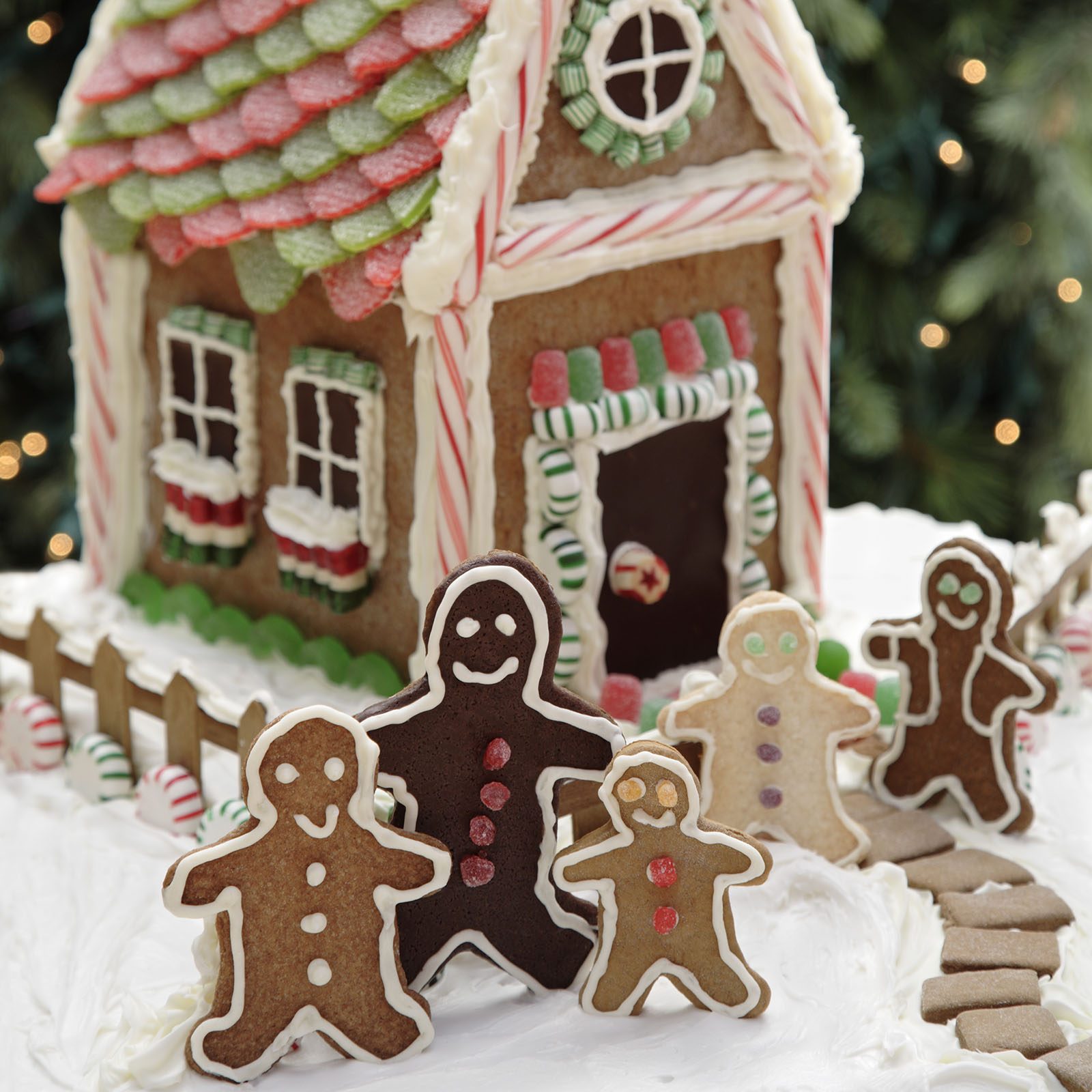 Gingerbread people smile, stand in front of a candy-decorated house, with icing snow and a colorful roof, surrounded by a festive setting.