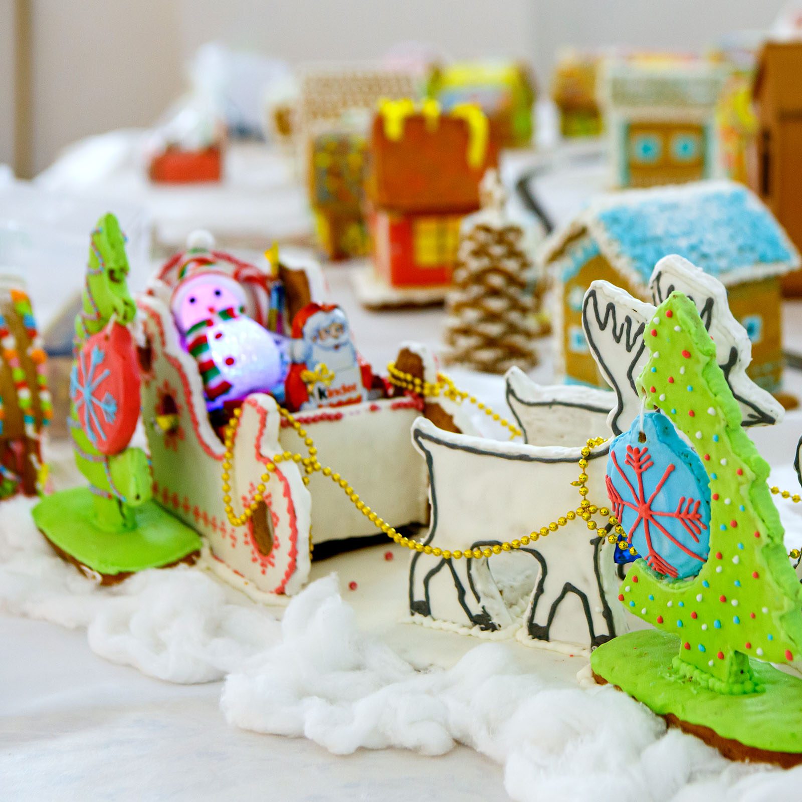 Gingerbread sleigh carrying candy figures through icing snow, surrounded by gingerbread houses and trees in a festive holiday setting.