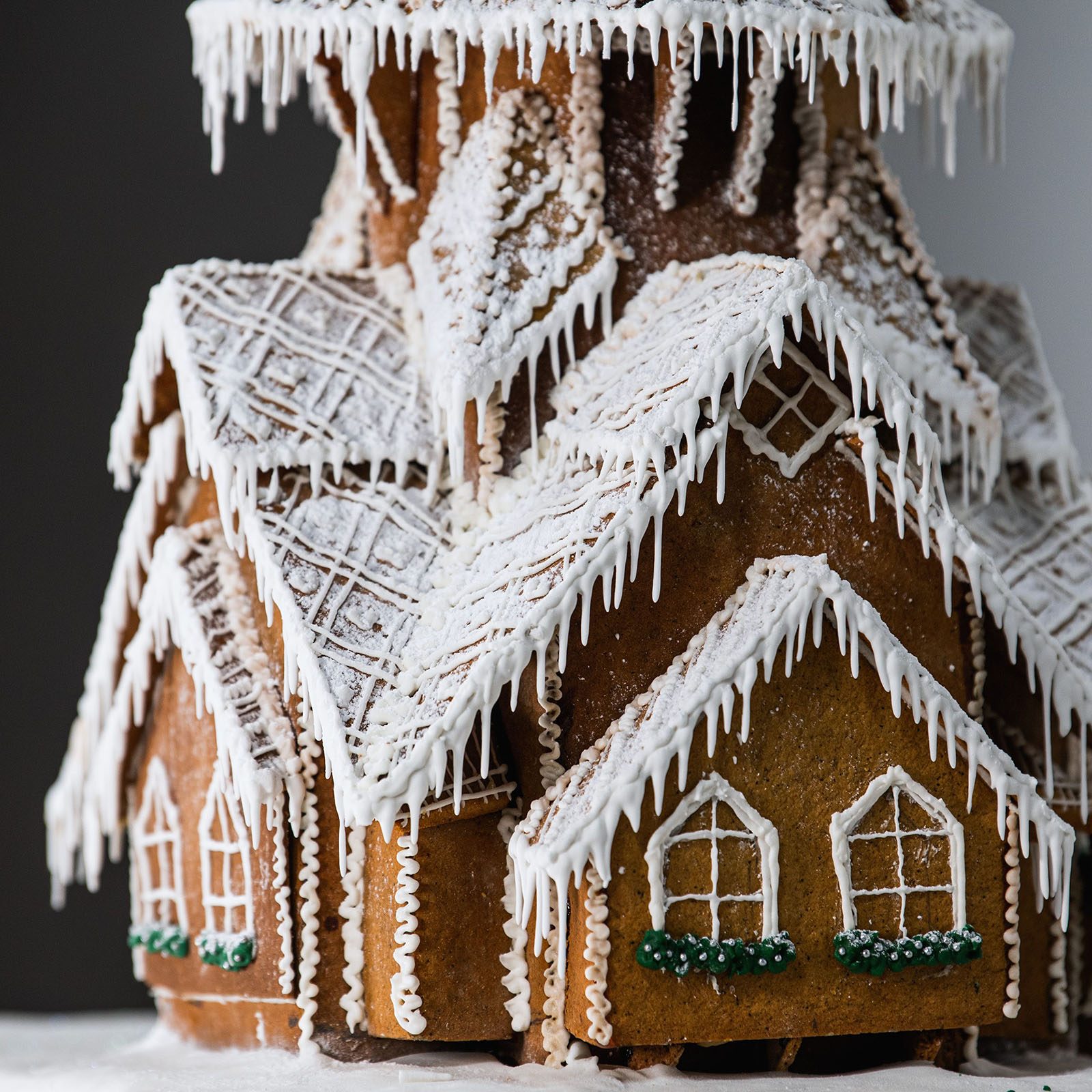 Gingerbread house displays intricate icing designs resembling snow and icicles, set against a dark background.