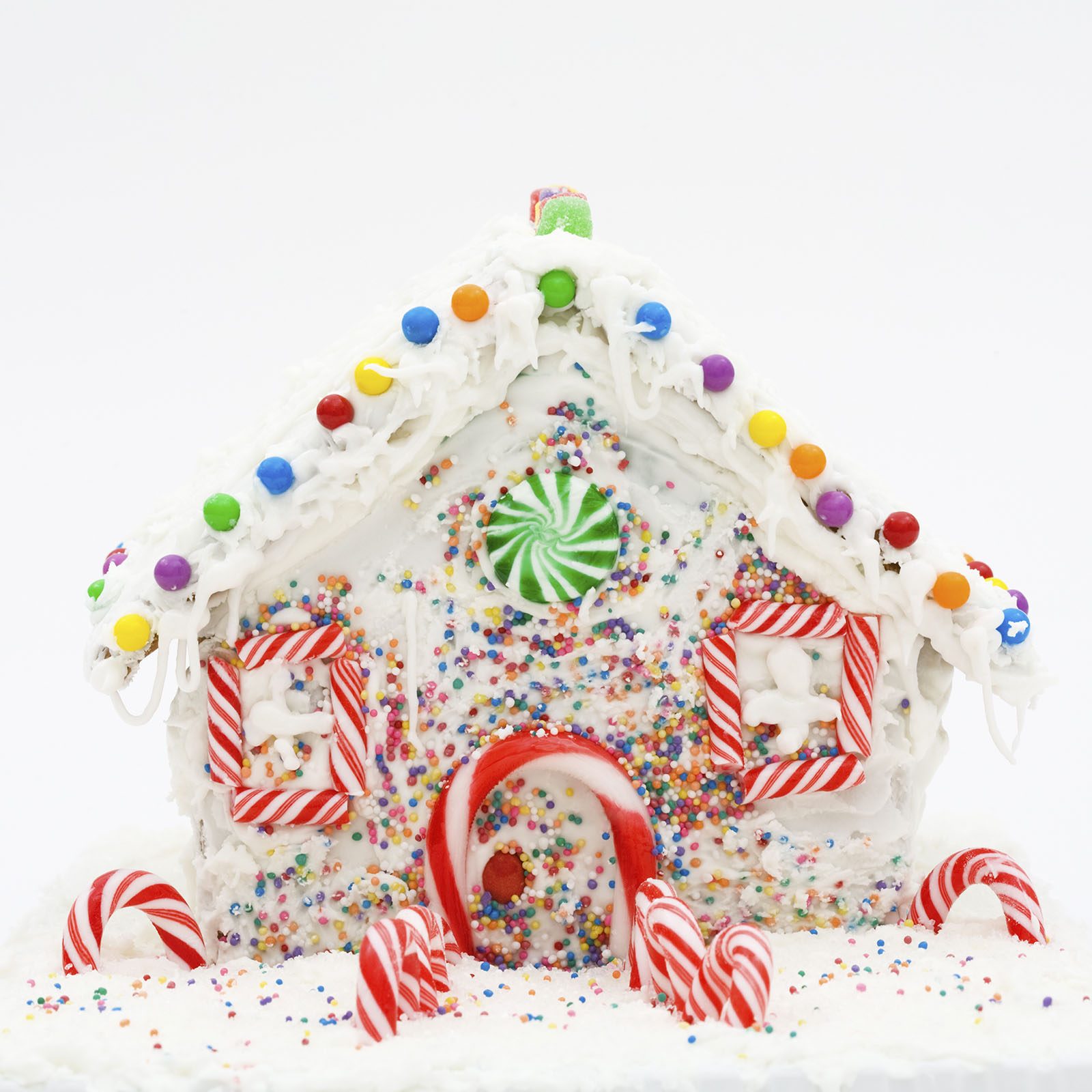 Gingerbread house decorated with icing, colorful candies, and candy canes, set against a plain white background.