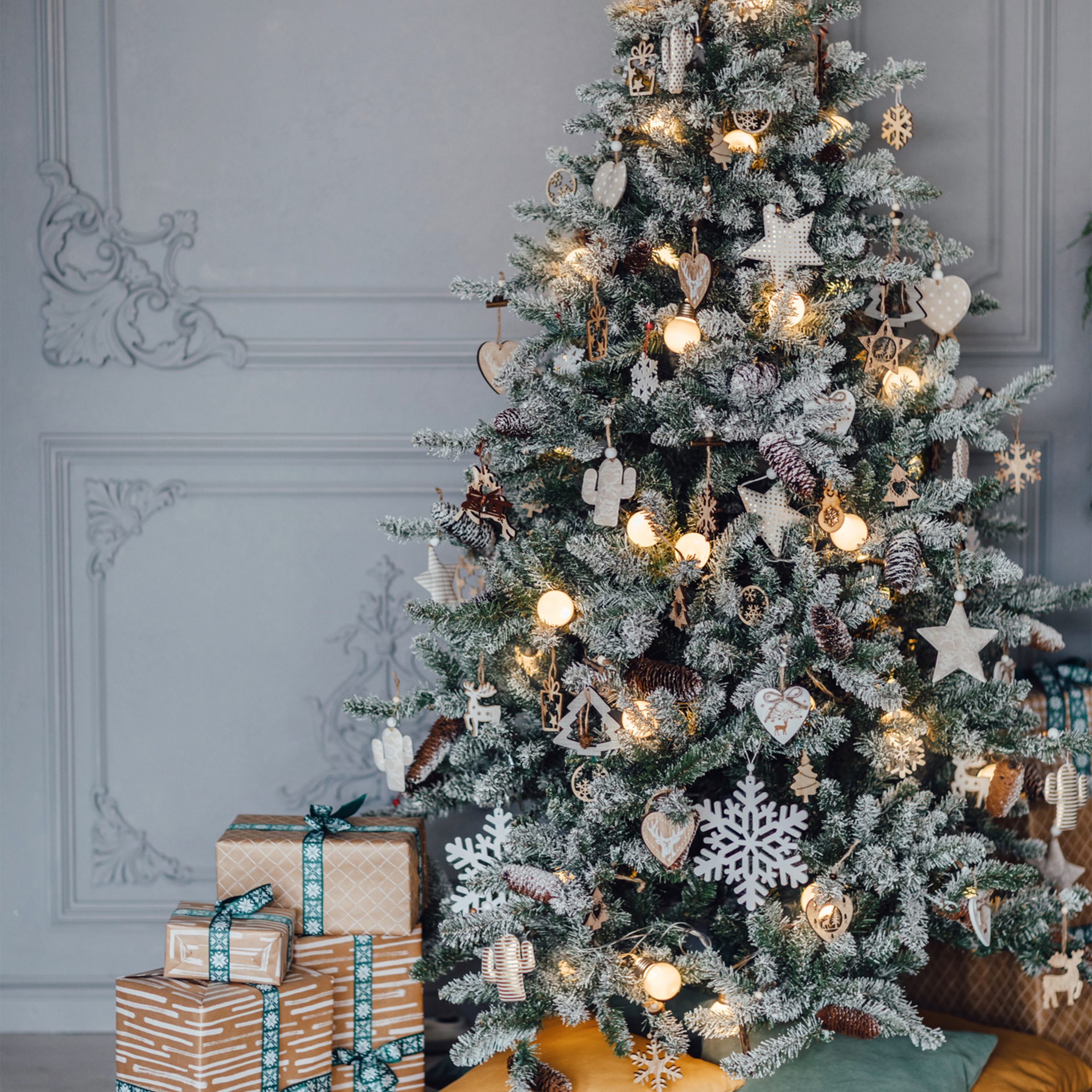 Decorated conifer christmas tree and gift boxes located near comfortable pillows in cozy room during Christmas celebration at home.