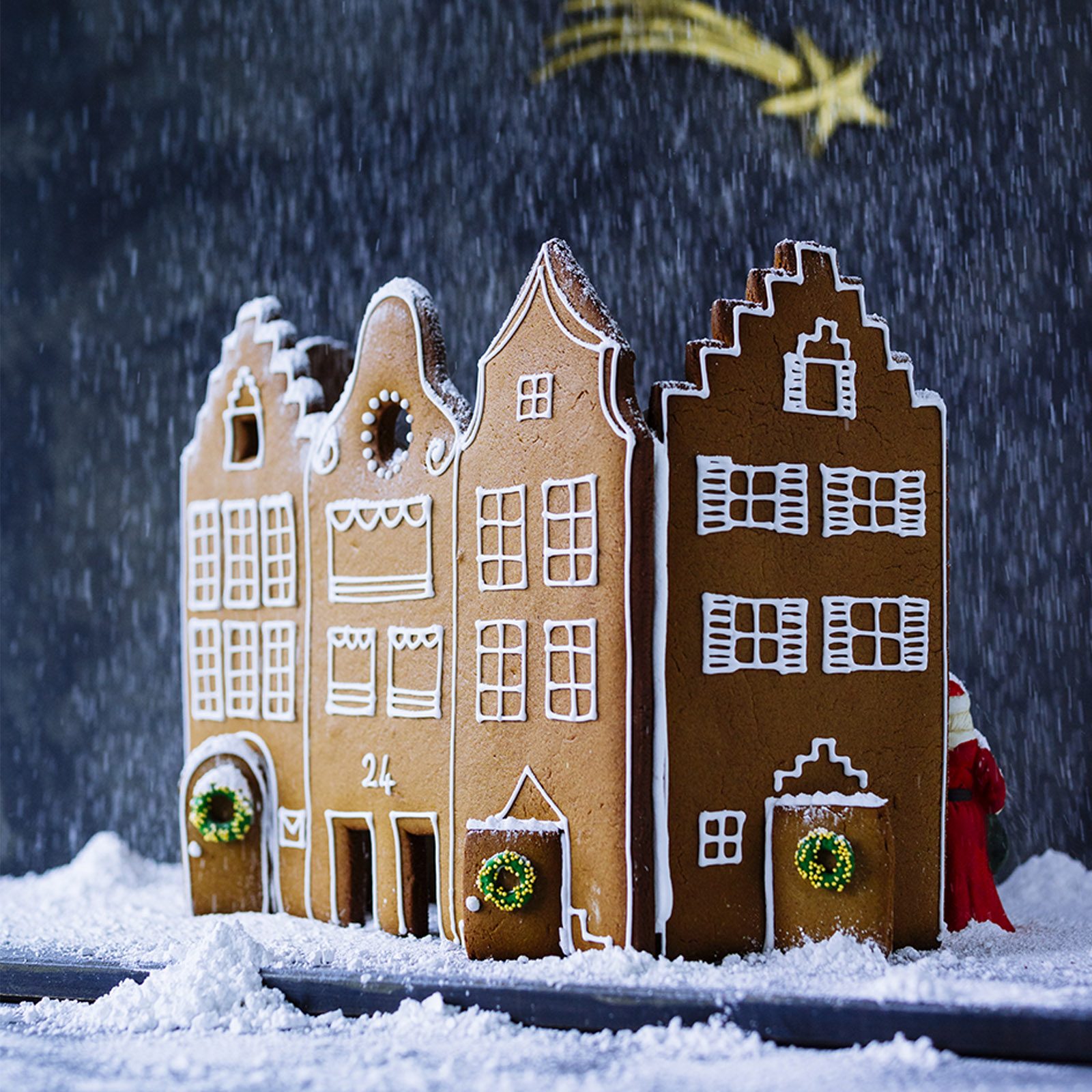Gingerbread houses stand dusted with powdered sugar resembling snow, set against a dark backdrop with a star, creating a festive scene.