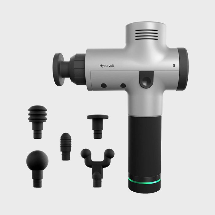 Massage gun displayed with six interchangeable attachment heads, set against a plain background. The side of the gun reads 