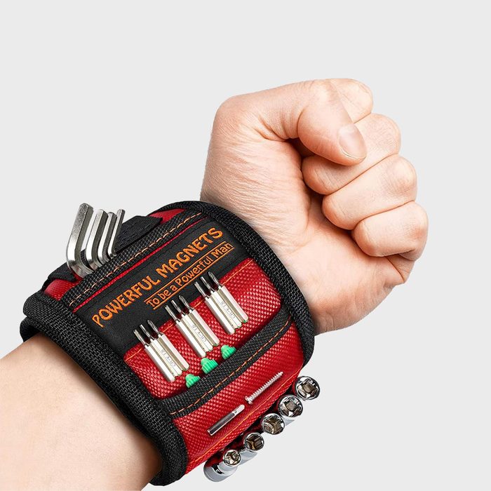 Wristband secures various tools and metal objects using magnets, worn on a clenched fist against a plain background. Text: 