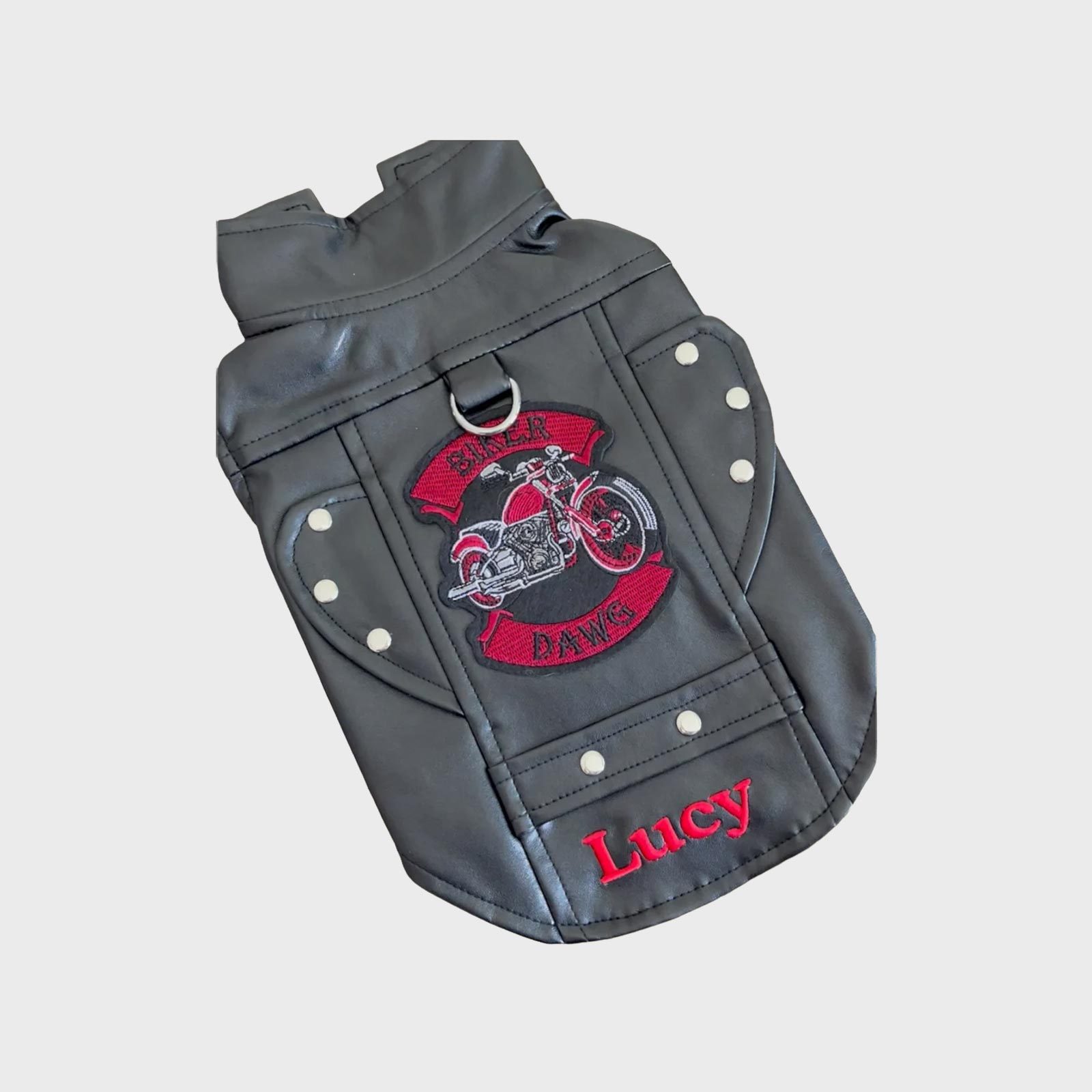 Dog motorcycle jacket displays red-embroidered motorcycle design, reads "Biker Dawg" and "Lucy," surrounded by studs on gray material.