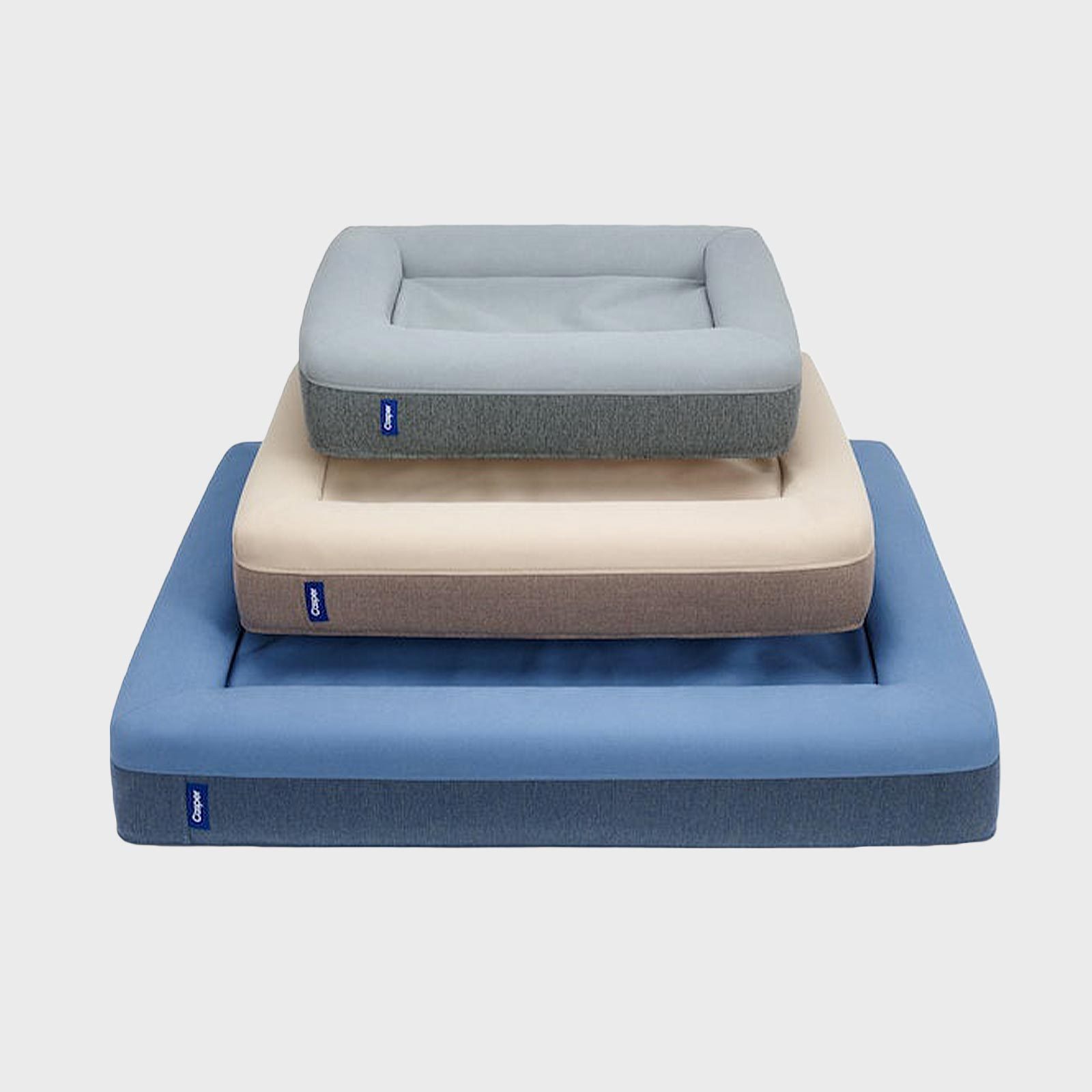 Three stacked, rectangular dog beds with side bolsters; arranged largest to smallest. They are colored blue, cream, and gray. Labels read "Casper."