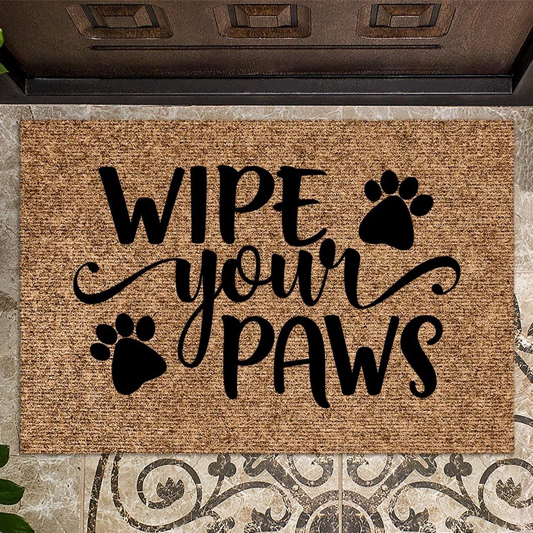 Doormat displays "WIPE your PAWS" with paw prints, resting on a patterned tile floor near a doorway.