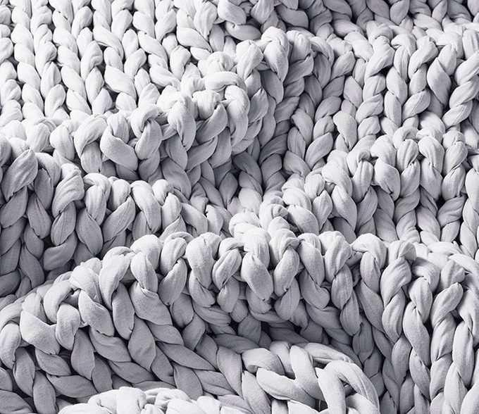 Chunky knit blanket rests with soft folds, displaying a textured and cozy pattern in a neutral space.