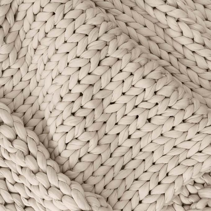 Chunky knit blanket drapes softly, displaying intricate braided patterns in a cozy, neutral-toned setting.