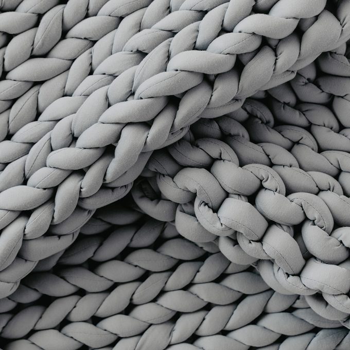 Gray chunky knit blanket, lying in loose folds, creating a cozy and textured appearance.