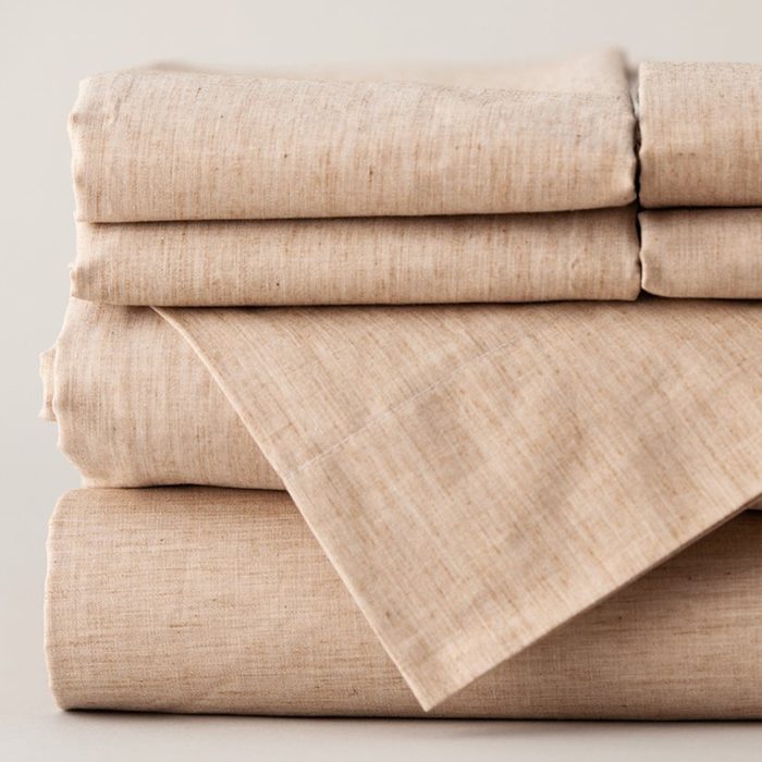 Beige bed sheets folded neatly in a stack, resting on a plain surface.