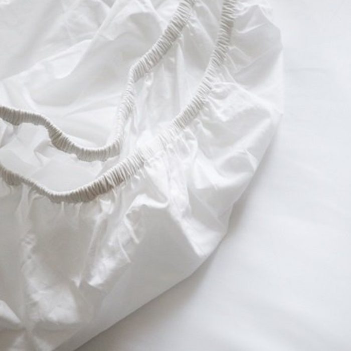 White fitted sheet lays crumpled, elastic edges exposed, on a smooth surface.