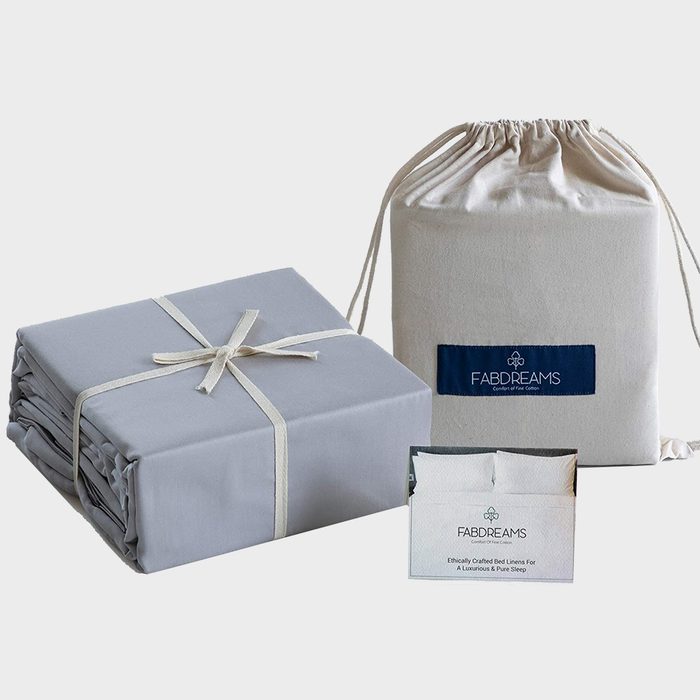 Folded sheets rest with ribbon, beside a drawstring bag labeled 