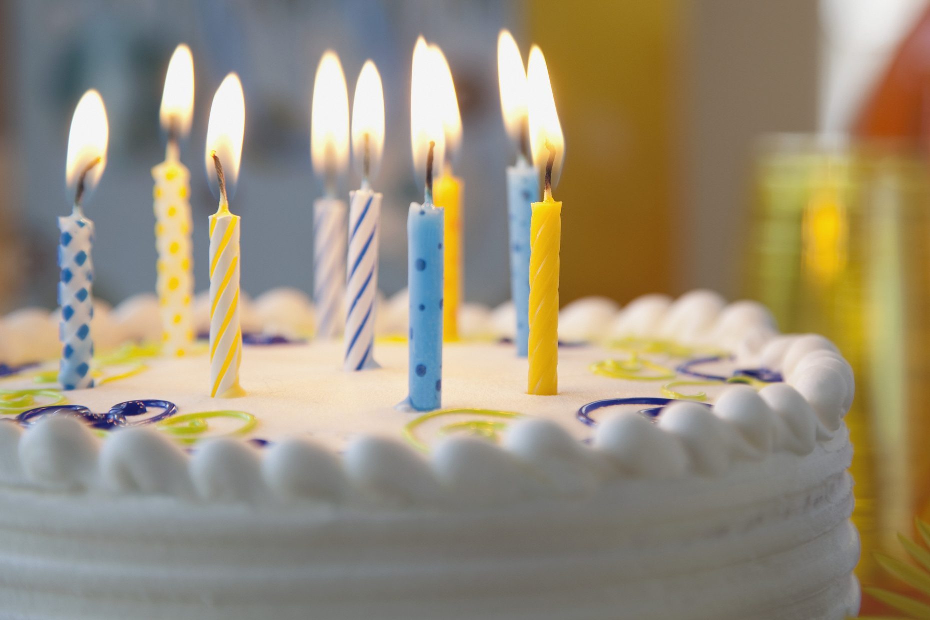 Colorful candles aflame atop a decorated white cake in a festive, blurred background.