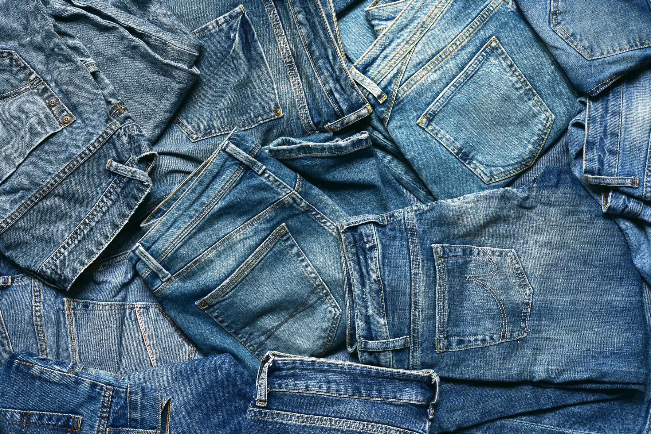 Denim jeans overlap, creating a textured pattern of various shades of blue against a flat surface.