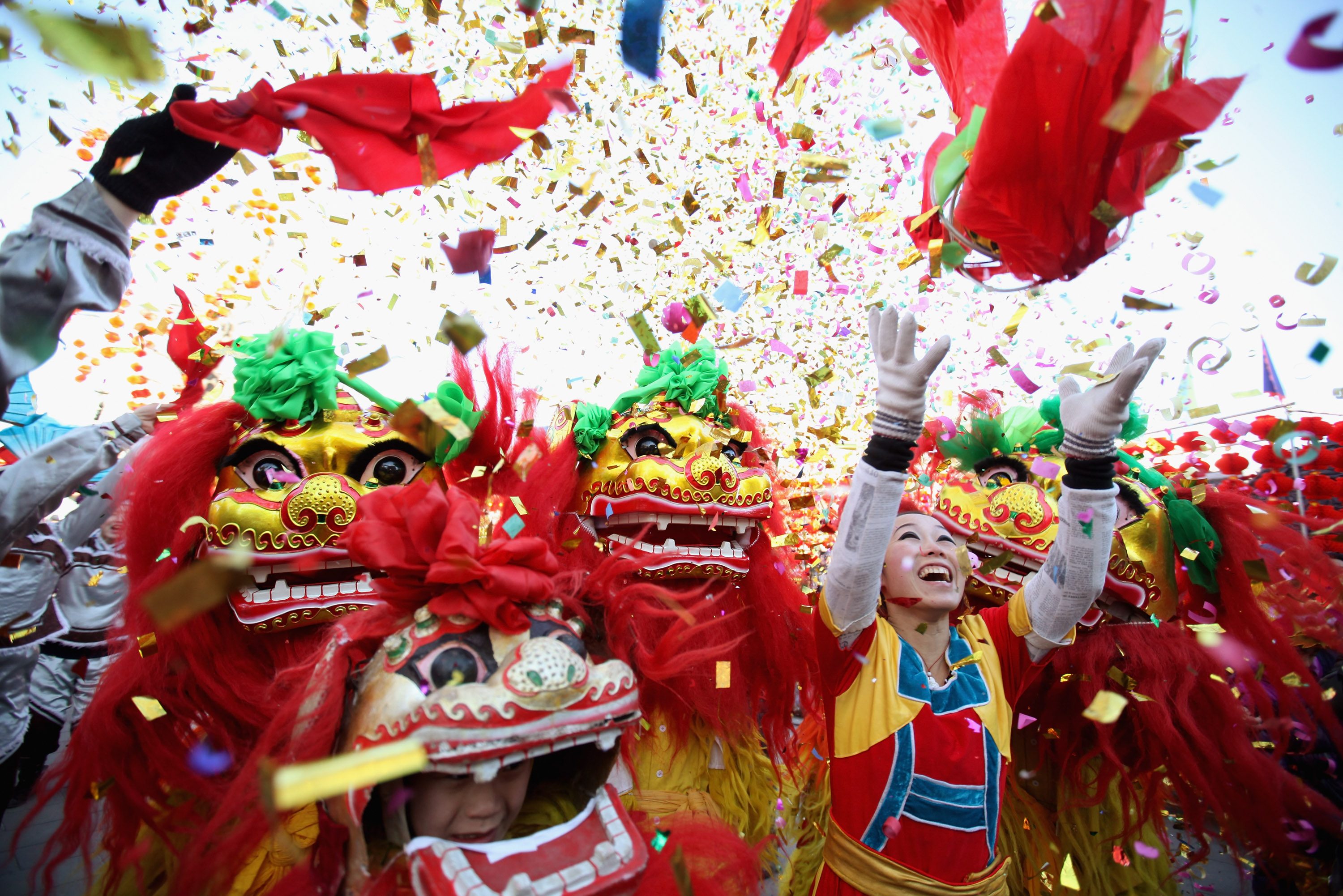 Lion dancers celebrate joyfully under a colorful confetti shower, with bright costumes and festive atmosphere surrounding them.