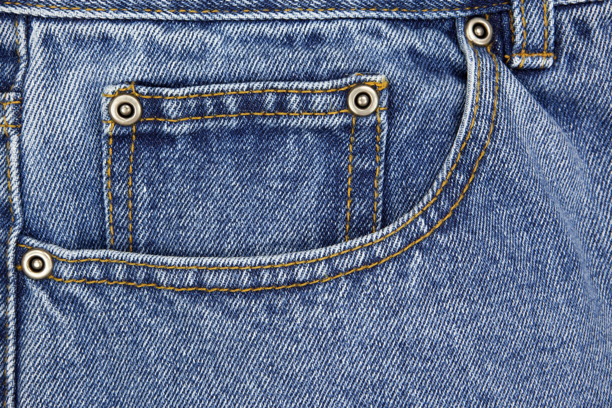 Denim pocket with metal rivets, stitched with yellow thread, close-up view showing texture and seam details of blue jeans fabric.